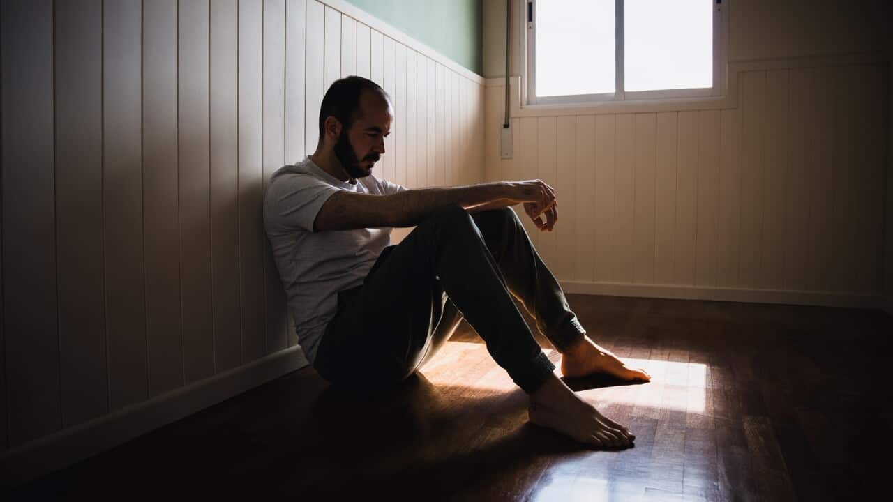 Lonely man sitting on floor by wall in dark room feeling sad