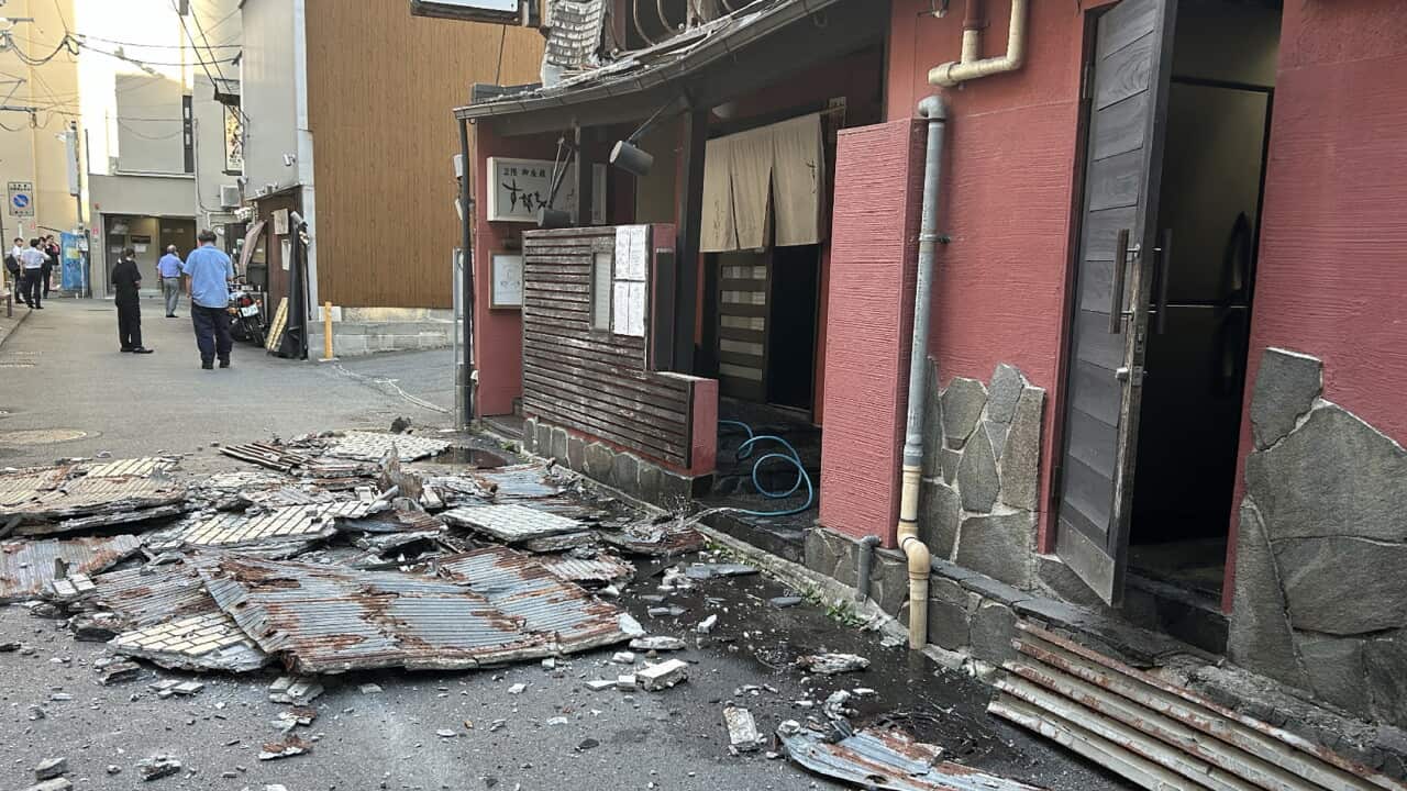 A piece of wall smashed on the ground next to a red building in a side street