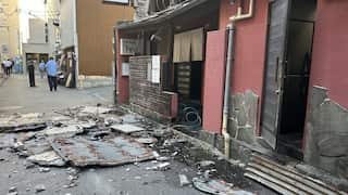 A piece of wall smashed on the ground next to a red building in a side street