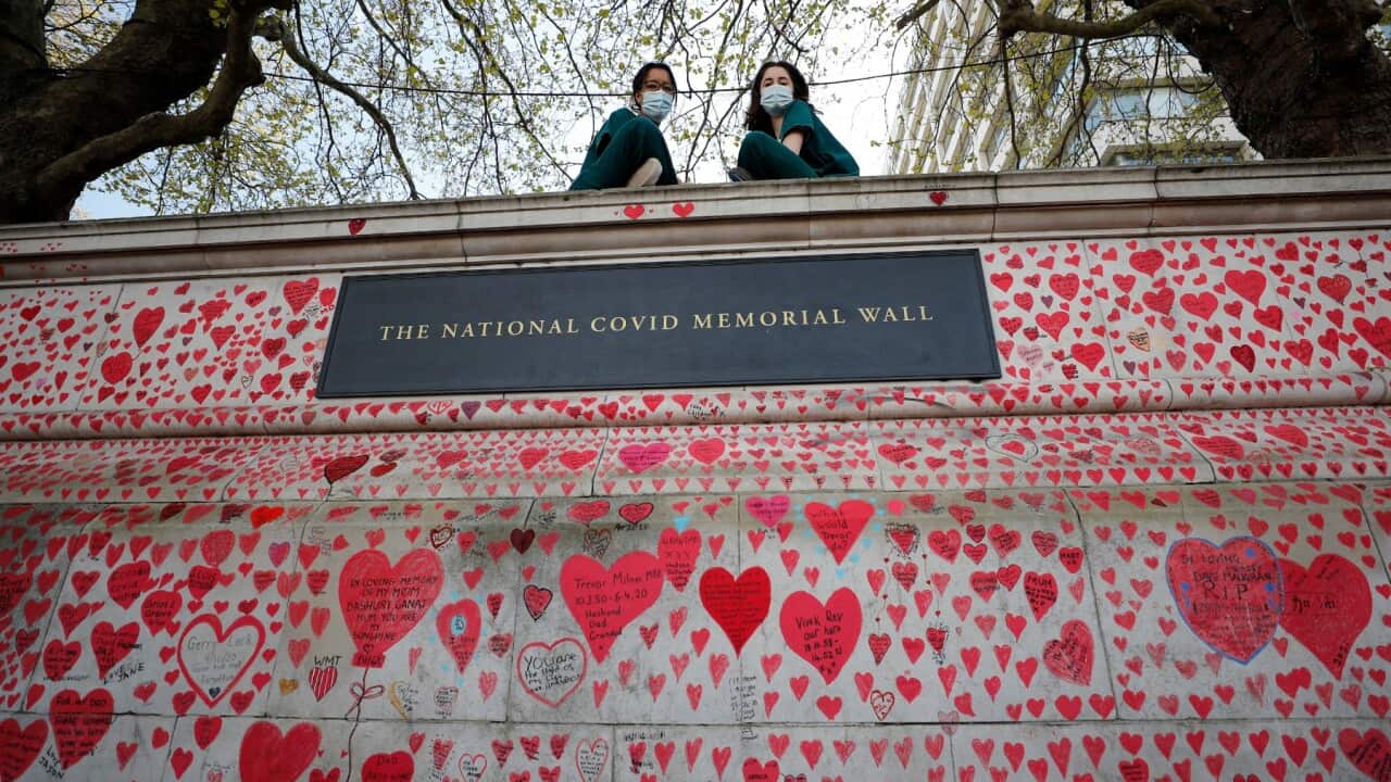 Nurses from the nearby St Thomas' hospital sit atop the National Covid Memorial Wall in London,