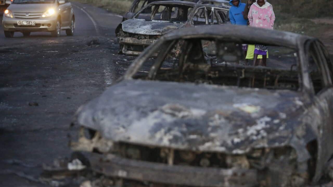 People walk amongst burned down cars