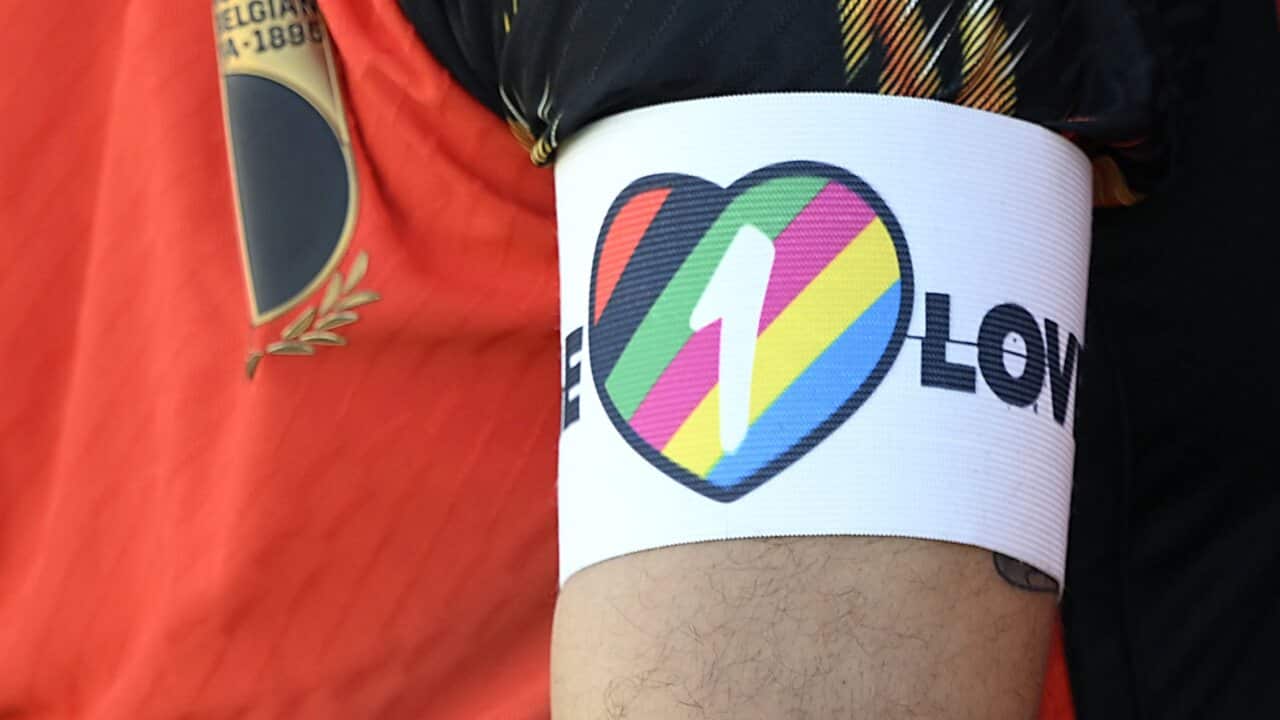A football player wearing an armband that features a heart filled in with rainbow colours and the number "1".