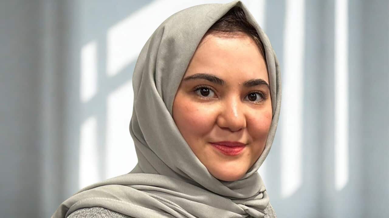 A young woman in a grey headscarf smiles at the camera