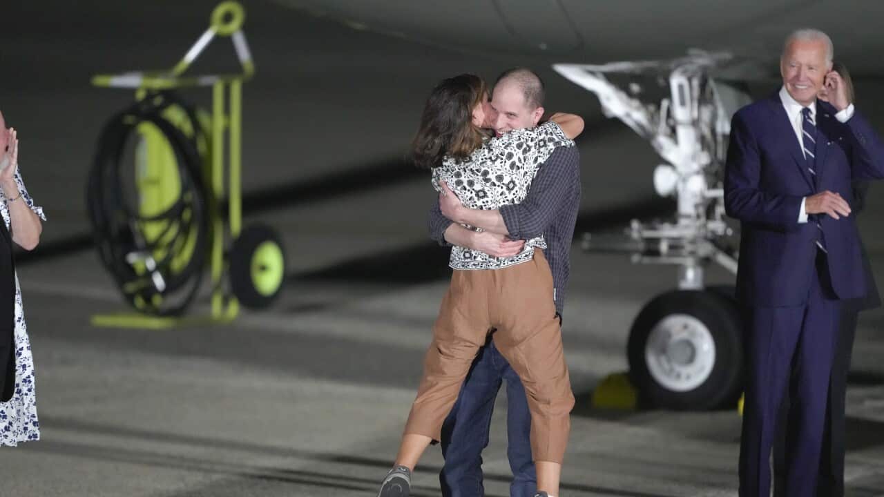 A woman in brown pants in raised in the air as she hugs a smiling younger man.