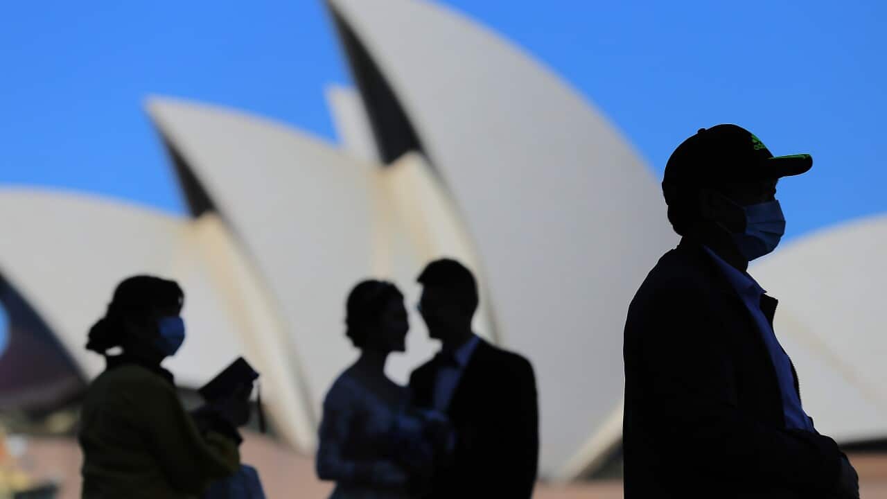 People wear face masks in front of the Sydney Opera House.