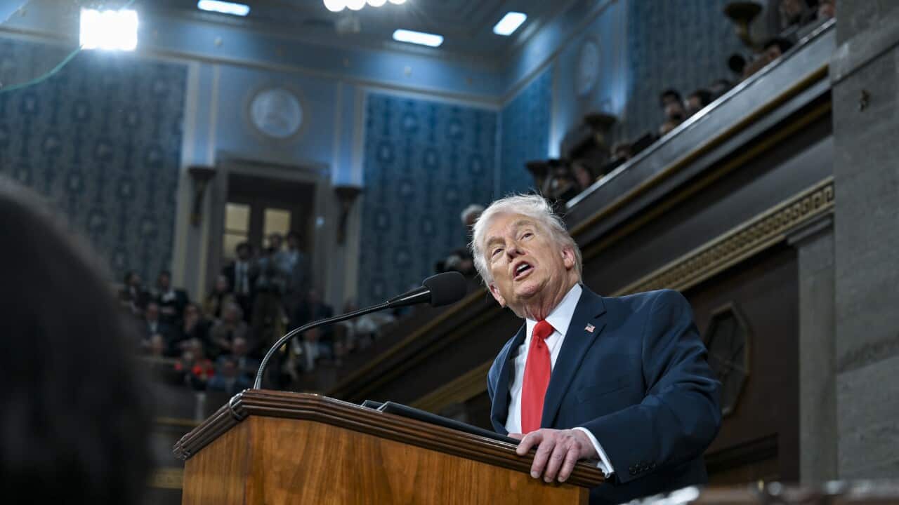 Donald Trump standing at a podium, speaking into a microphone, in a large hall.