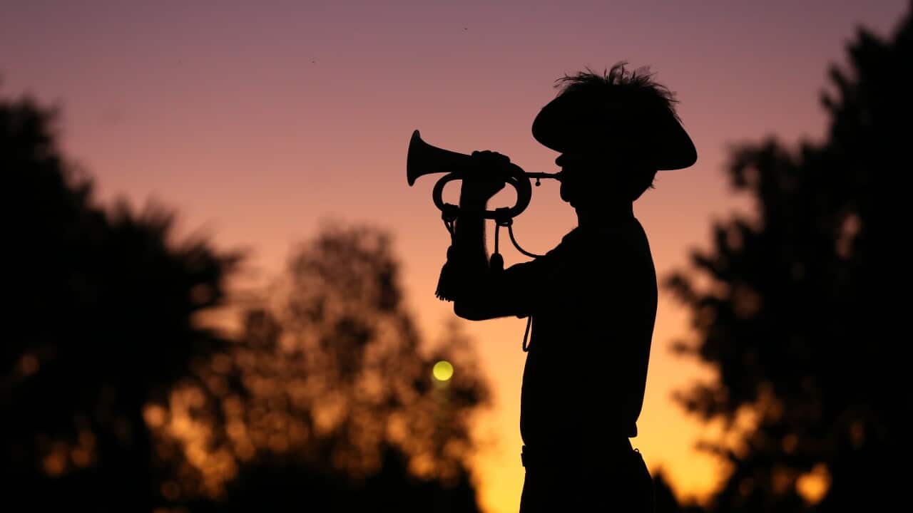 The silhouette of a man wearing a hat, playing a bugle at sunrise.