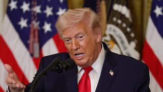 Trump speaking at a microphone with the US flag behind him.