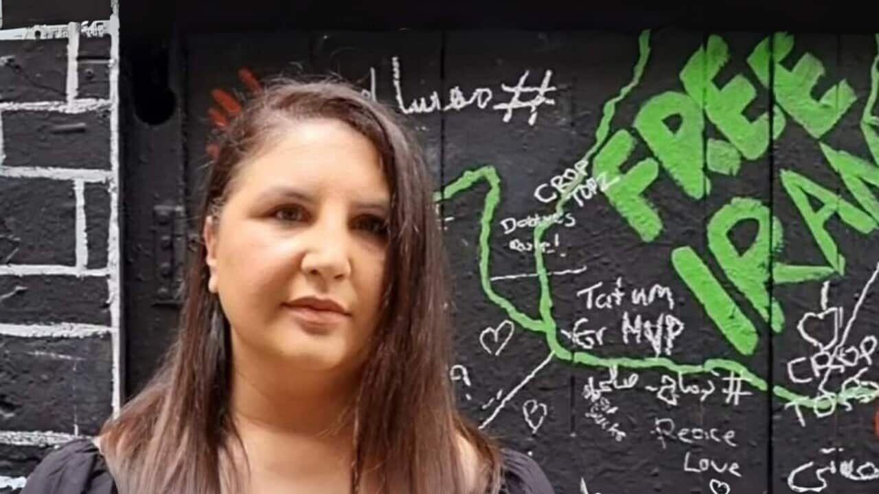 Nos Hosseini stands in front of a wall with graffiti on it.