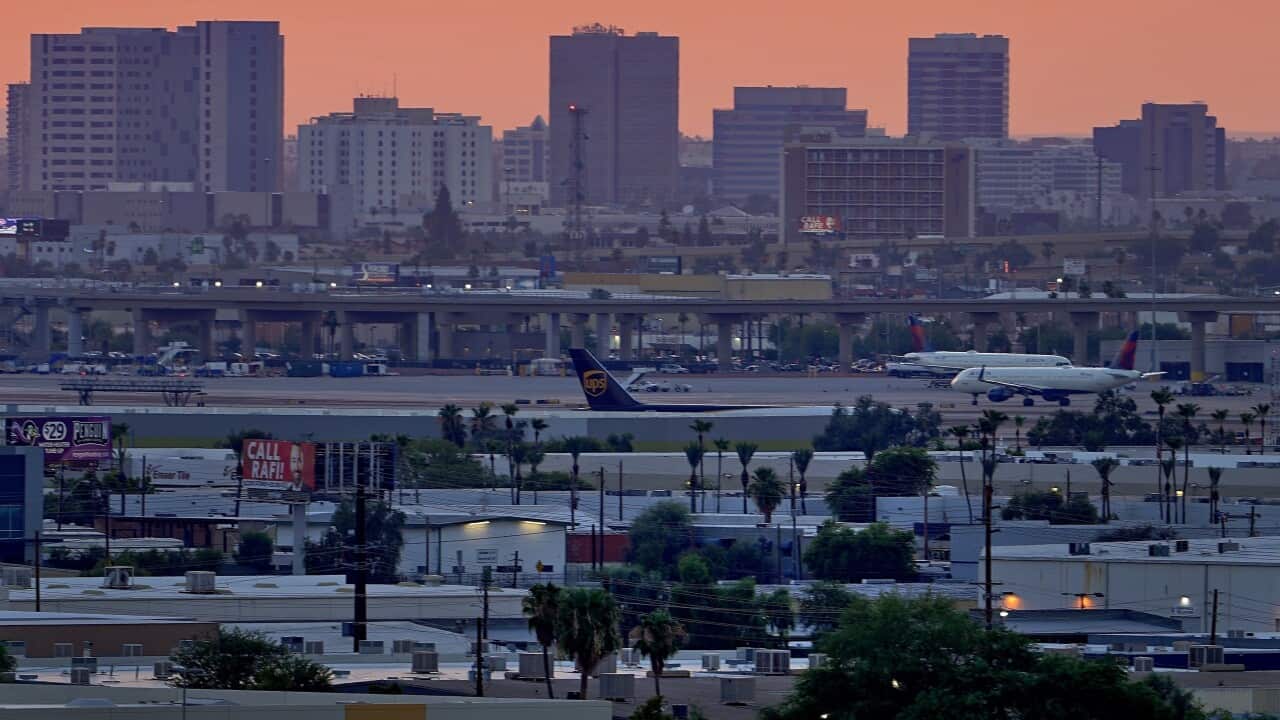 A sign displays an unofficial temperature as jets taxi at the runway of an airport at dusk.