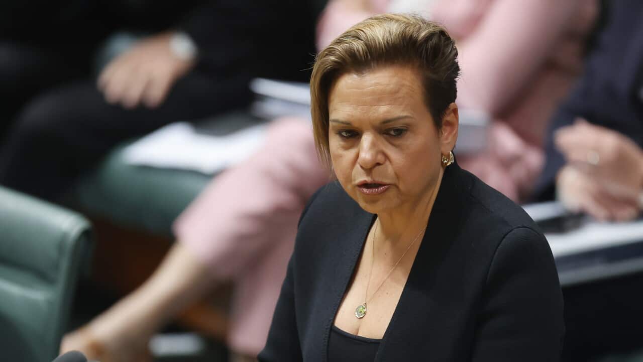 A woman in a black blazer speaks into a microphone.
