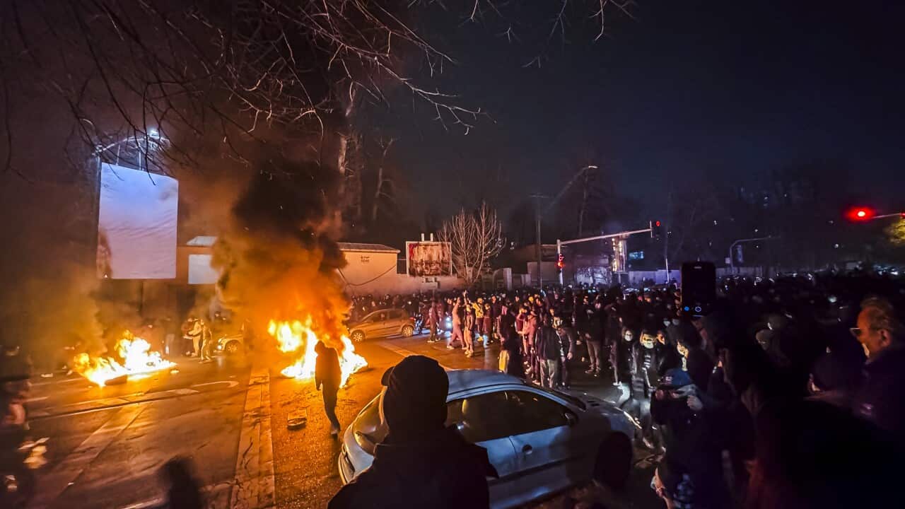 Protesters stand around burning objects on a street.