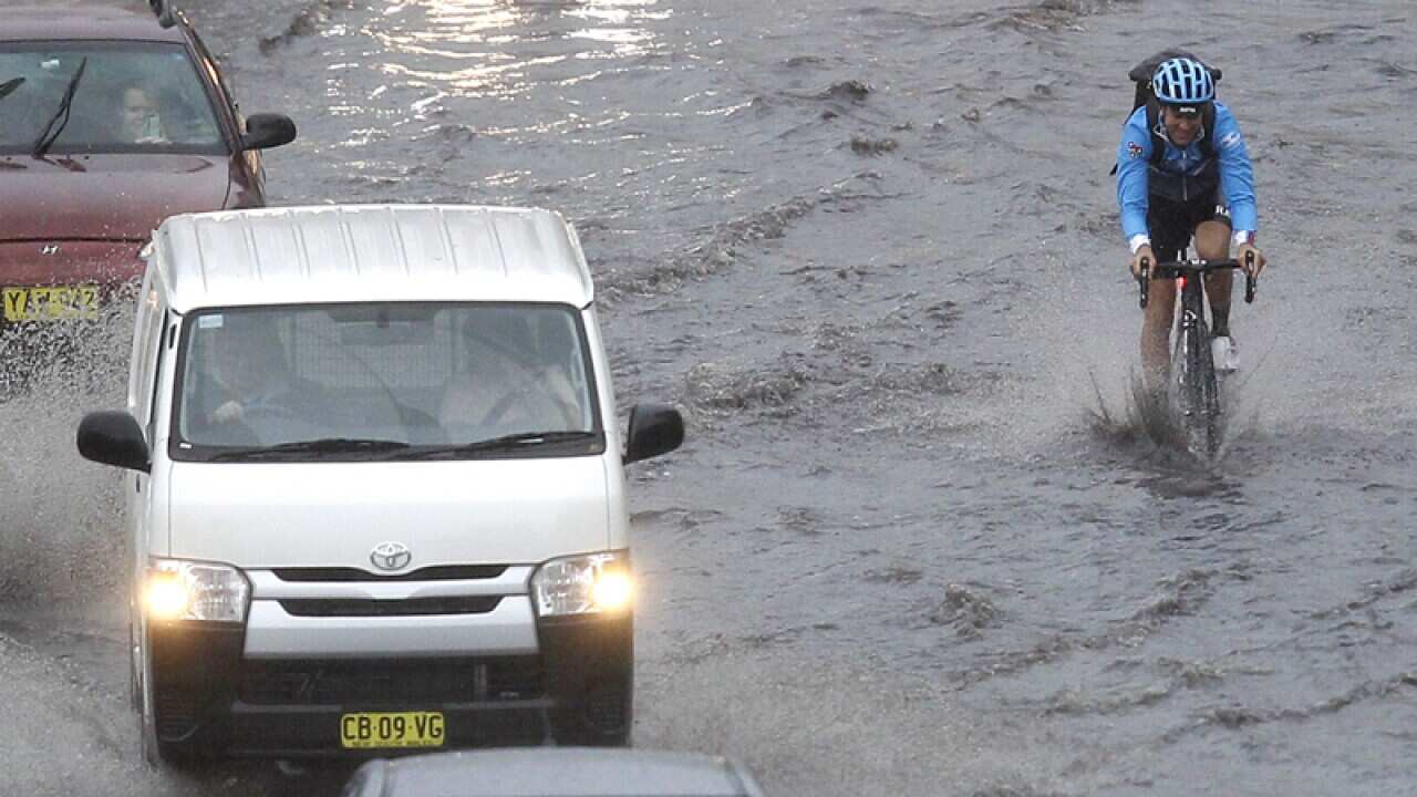 A cyclist smiles as he powers his way through a flooded road in Sydney