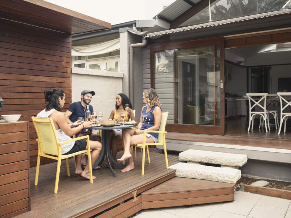 Group of four young adults relaxing on patio outside house with food and drink