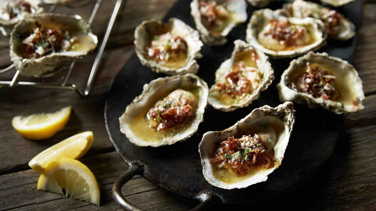 Juicy oysters sit on a round black metal tray, with slices of lemon alongside.