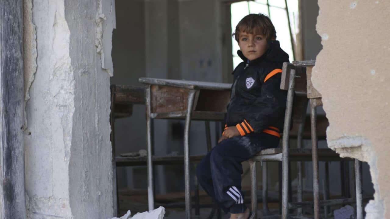 A Syrian boy Ahmed, 6, sits on a damaged classroom school