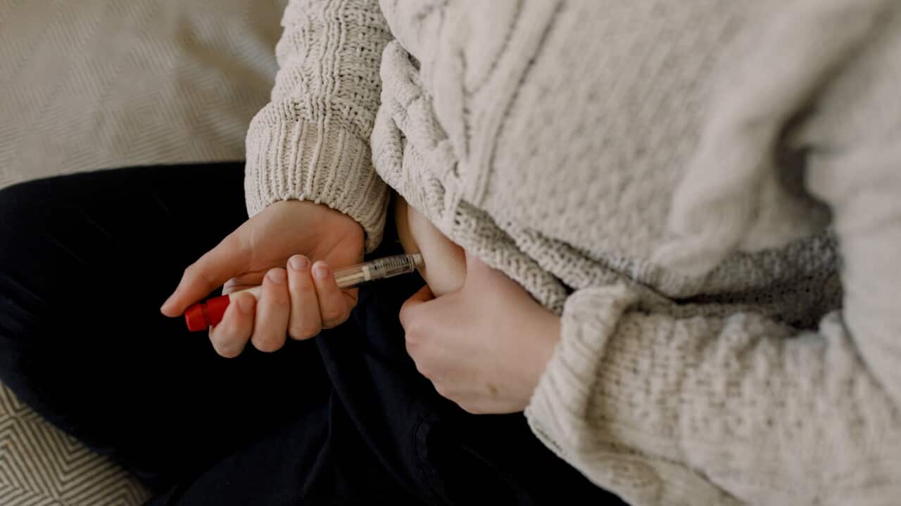 A woman injecting a syringe into her stomach.