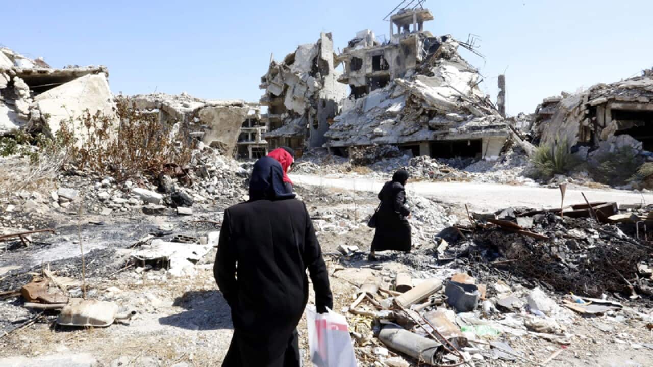People walk between rubble in the city of Homs, Syria