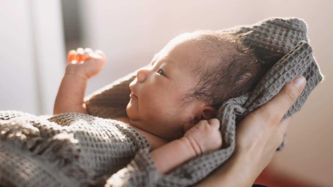 Cropped shot of an Asian mother holding a newborn baby wrapped in a towel.