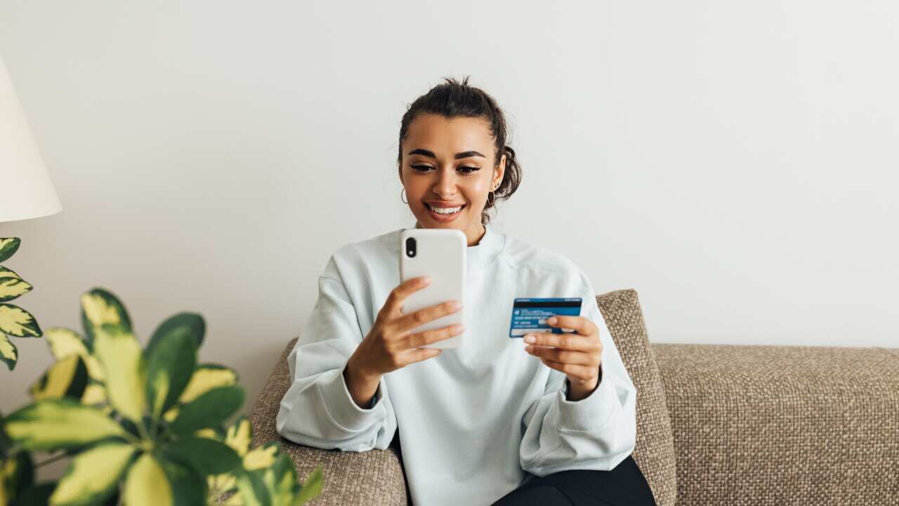 Smiling Woman Holding Credit Card While Using Smart Phone At Home