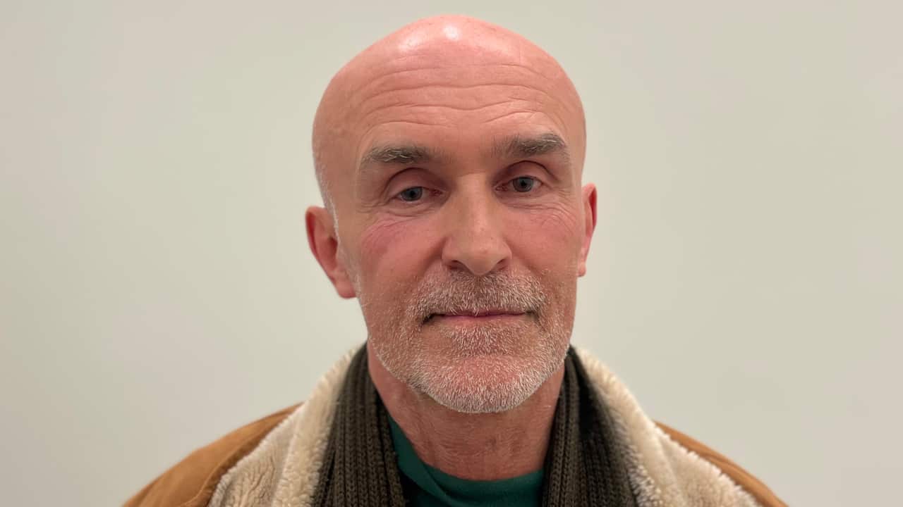 a closeup photo of an older bald man with grey stubble