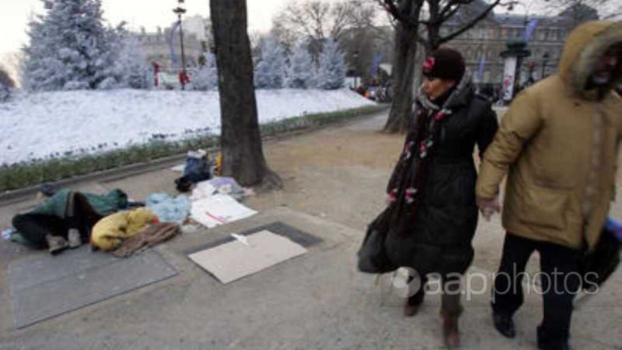 A woman looks at a homeless man sleeping at the Champs-Elysees round about in Paris,