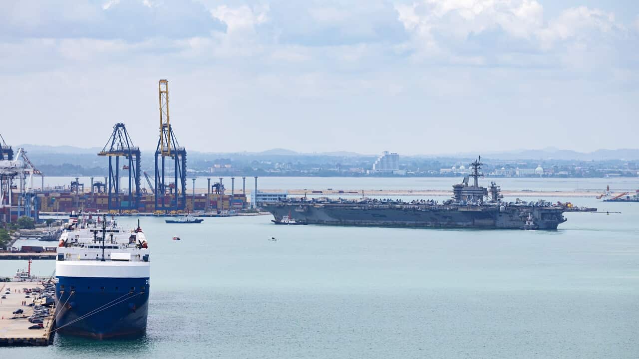 A large navy ship arrives at a dock
