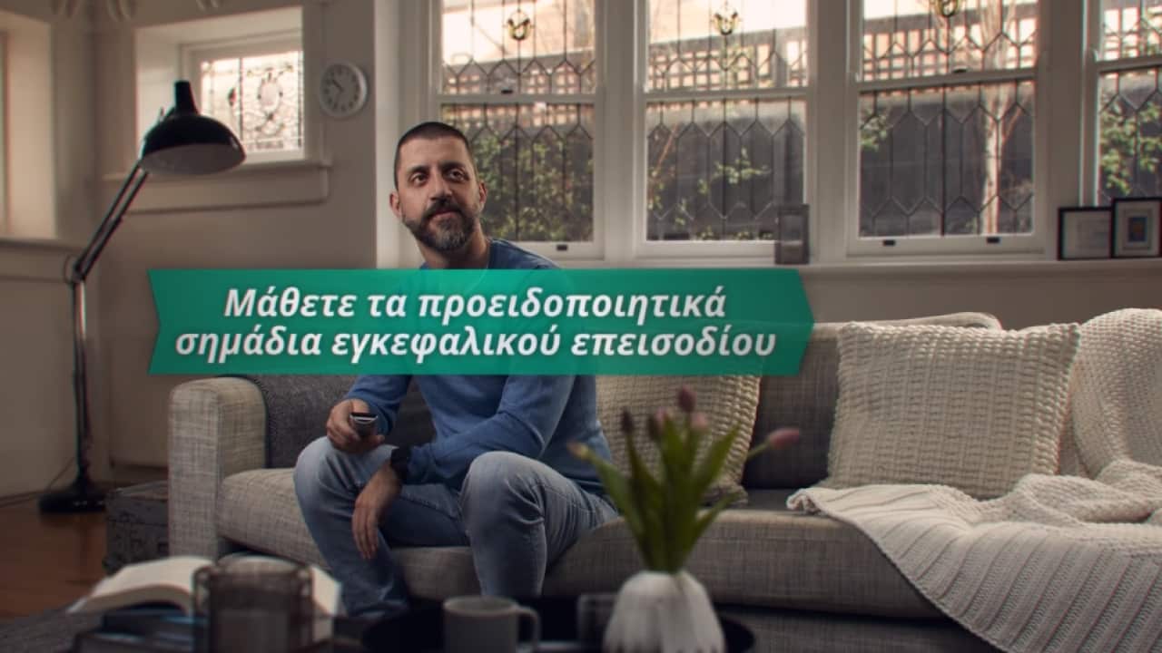 Bill Gasiamis sits on couch at home holding TV remote