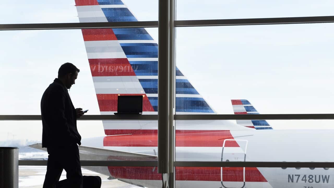 A silhouette of a man holding a phone and with a laptop in front of a window with a large aeroplane in the background.