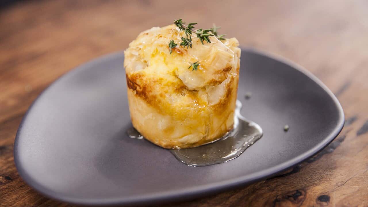 A round golden pie sits on a wide plate in a small pool of syrup.