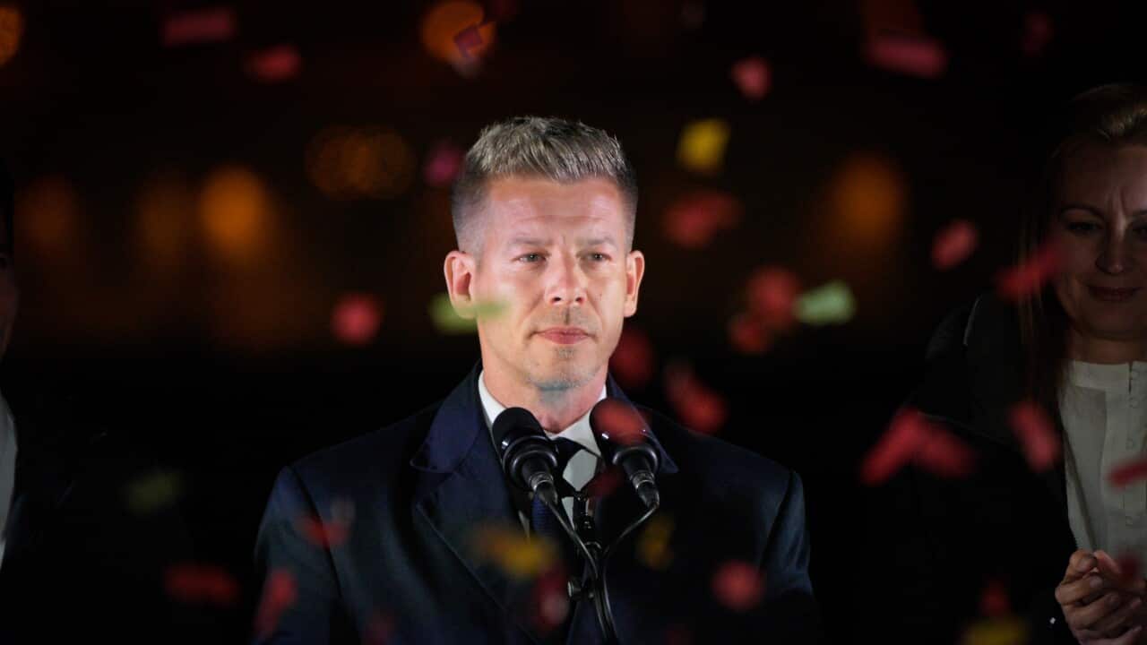 A man standing in front of two microphones, with colourful paper streamers surrounding him.