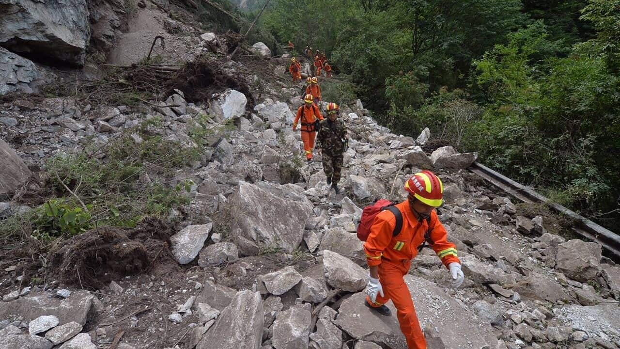 Chinese rescuers walk on a damaged cliff road to search for victims and survivors.