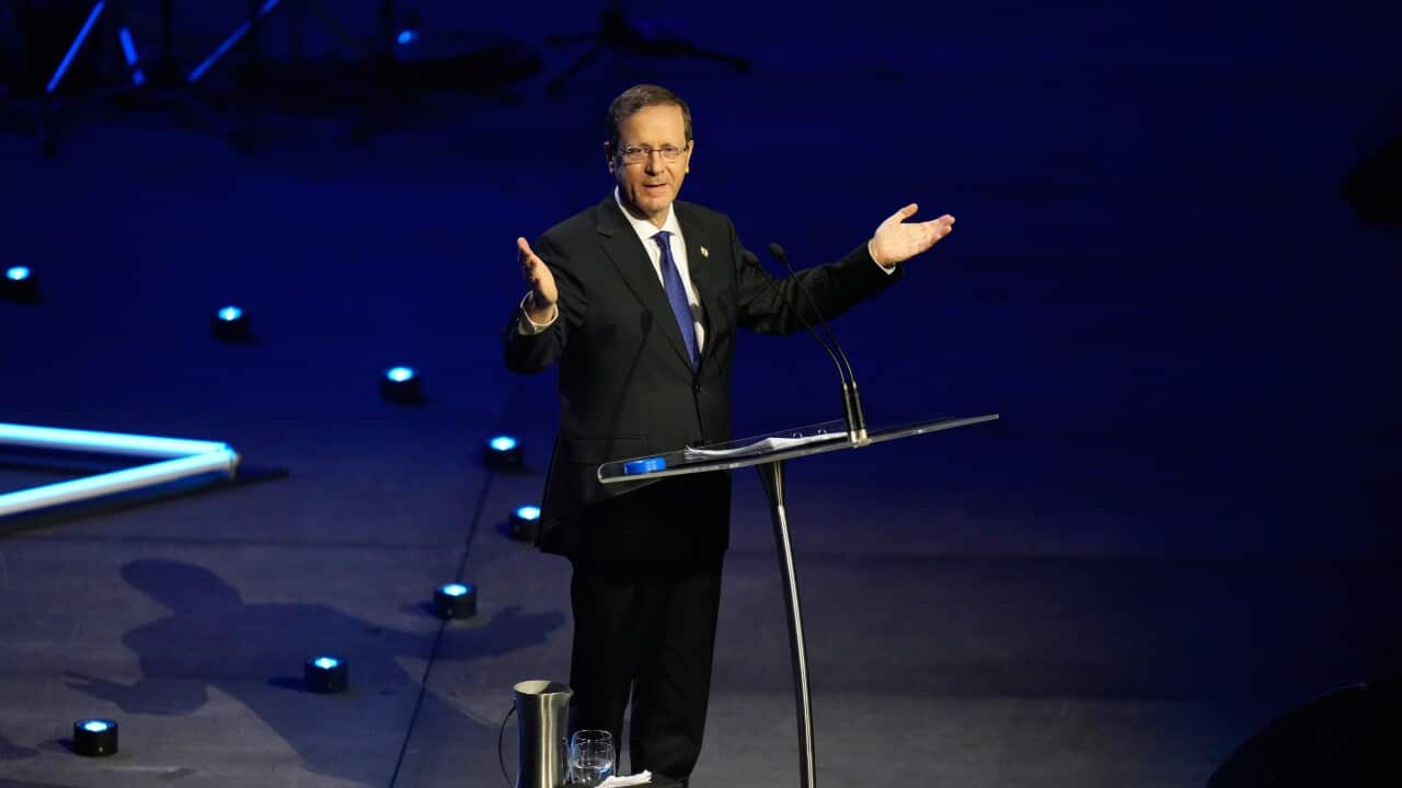 A white man in a black suit speaking on a stage before a lectern