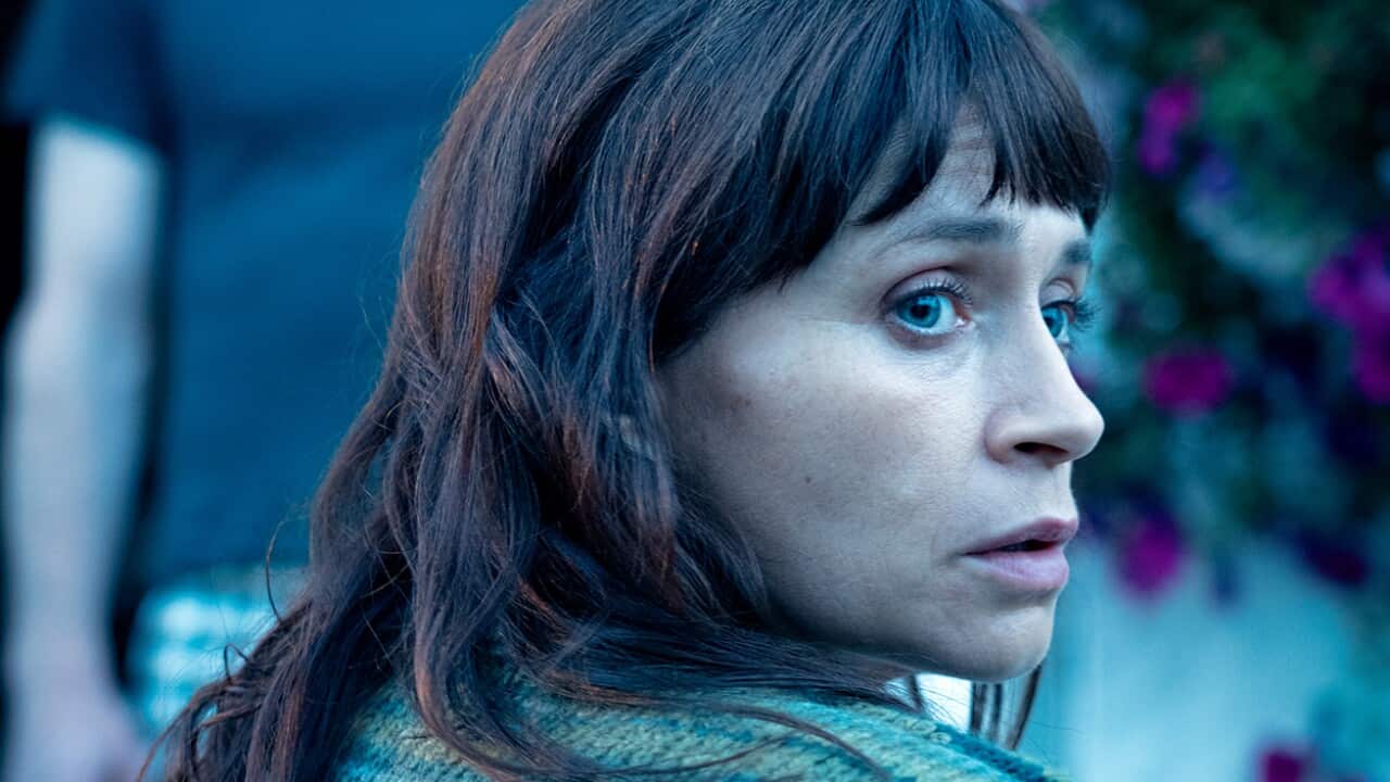 A woman with dark hair looks over her shoulder with a worried expression.