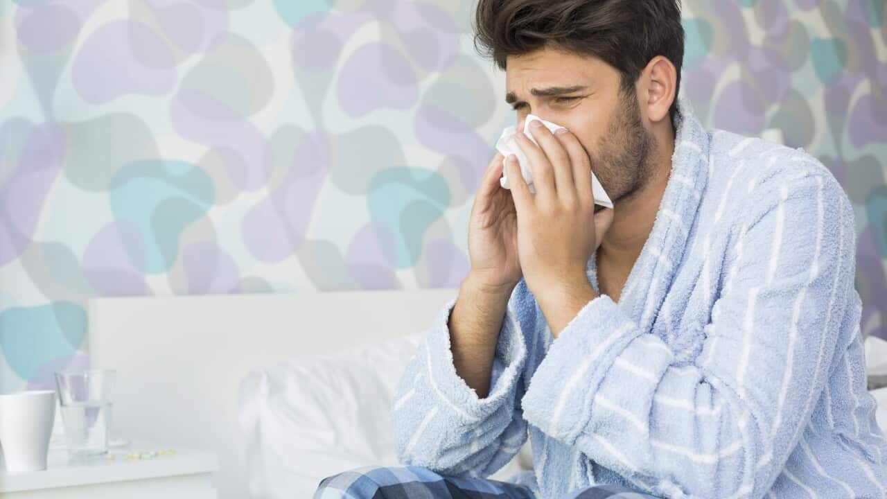 A sick man blowing his nose in tissue paper on a bed at home.