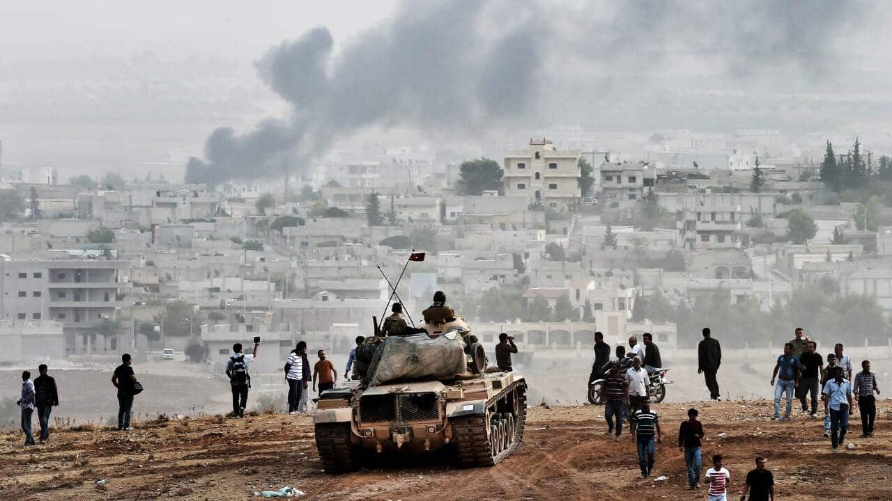 Turkish soldiers on a tank and Kurdish people look at Kobane