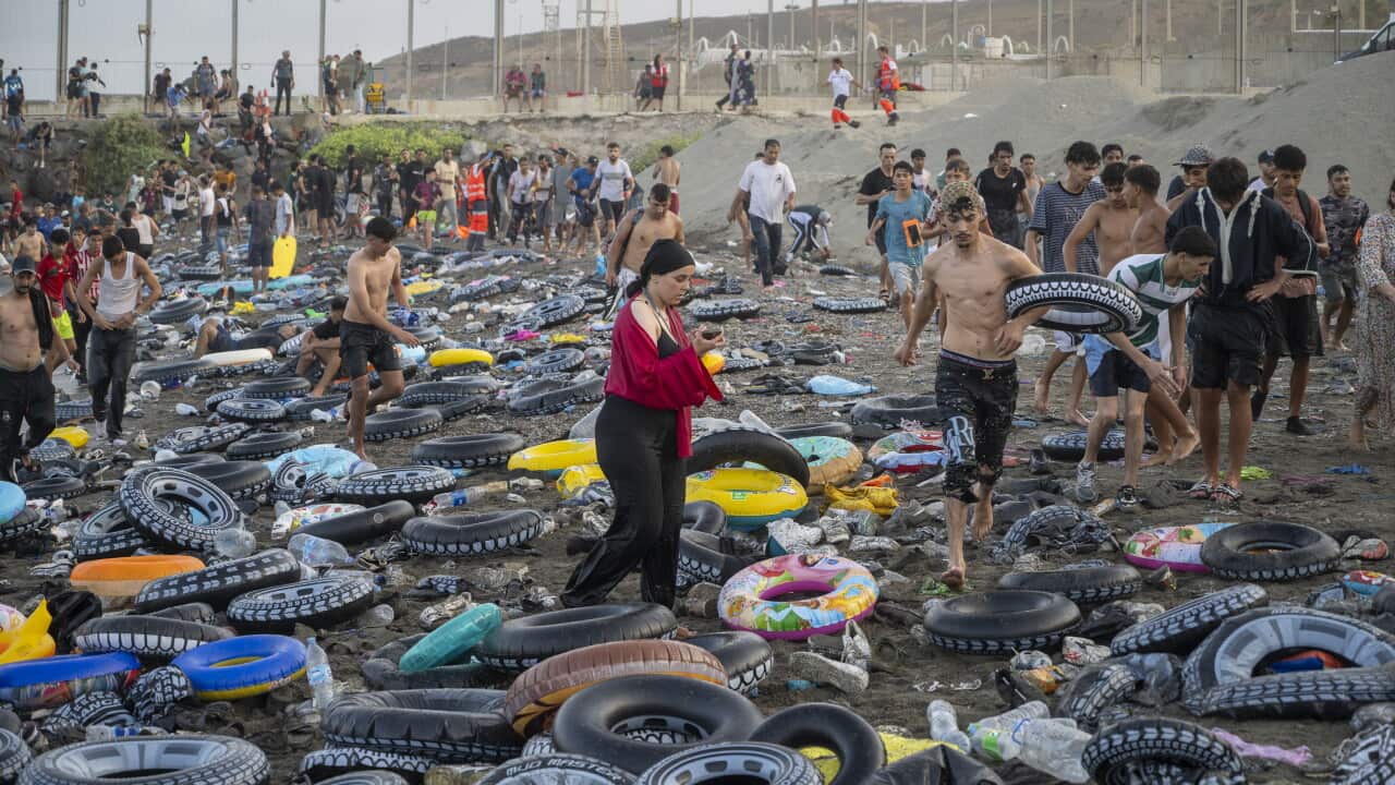 People walking on a beach covered with trash and rubber flotation rings.