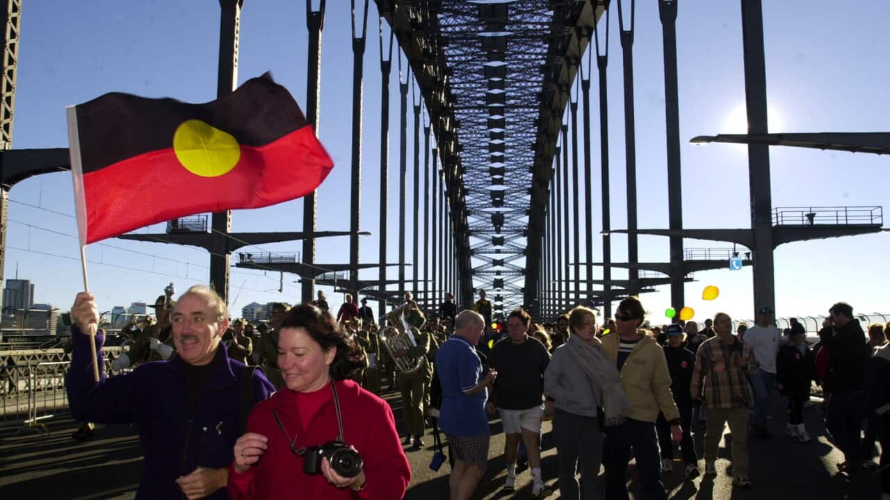 People walking across Sydney Harbour Bridge with the Aboriginal flag shown.
