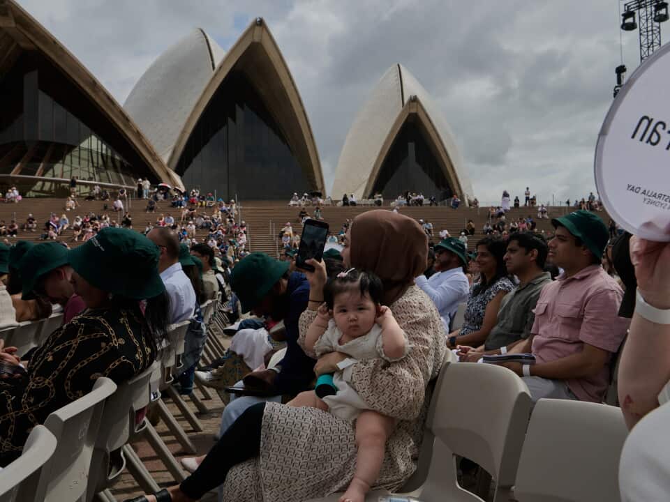 A mother holds a child in front of the Sydney Opera House for a citizenship ceremony