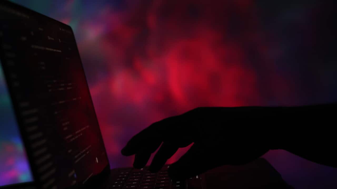 A stock image of code displayed on a computer screen with a hand approaching the keyboard.