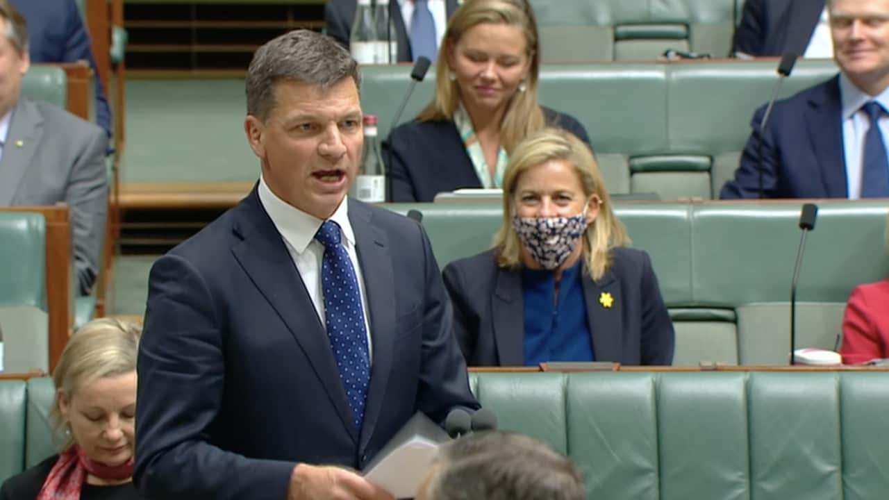 A man in a suit talks to others seated around him.