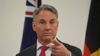 A man wearing a suit and a red tie points his finger as he speaks