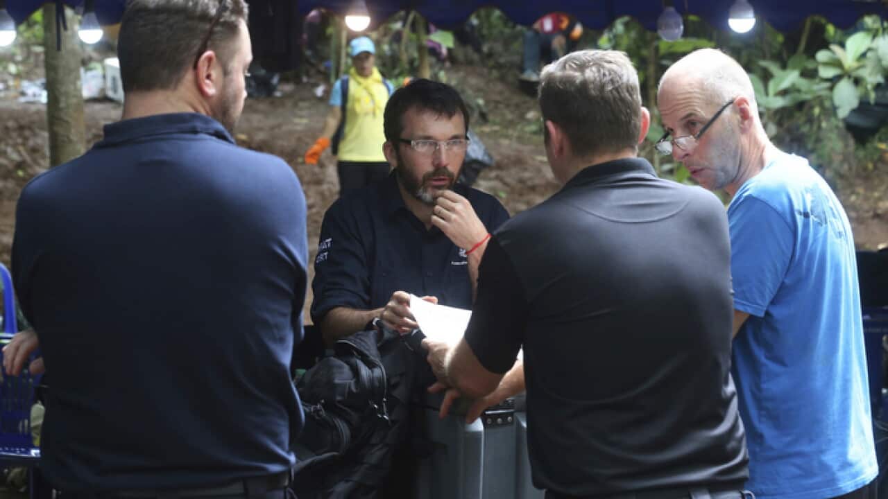 Australian Federal Police and Defense Force personnel talk each other near a cave where 12 boys and their soccer coach are trapped