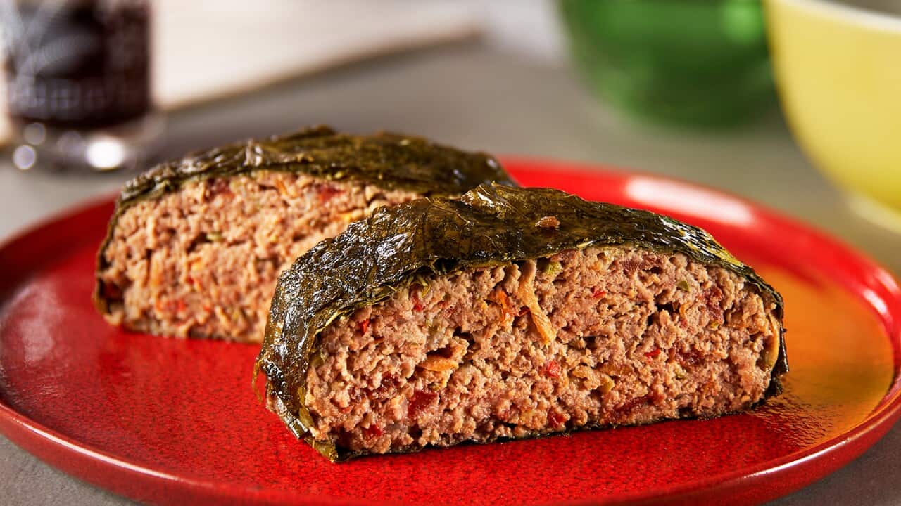 Two thick slices of meatloaf sit on a red plate, both wrapped in vine leaf (the vine leaf strip goes around the top, sides and bottom, so the sliced surface of the meatloaf can be seen.