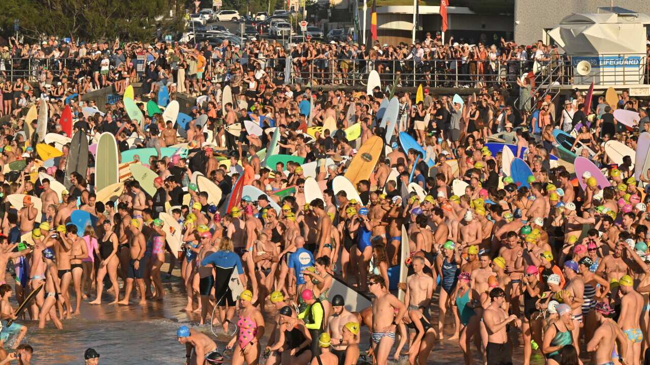 Large crowd gathered on the beach, many carrying boards.