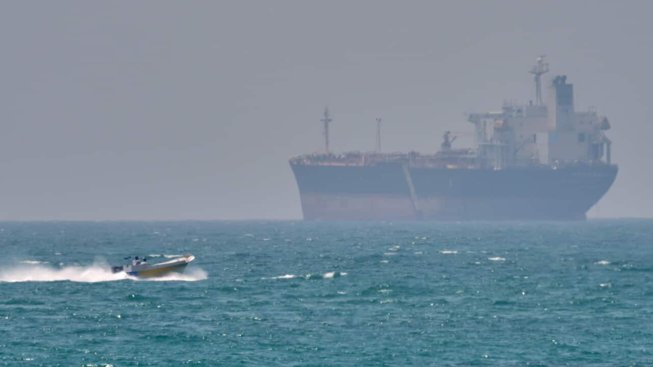 A speedboat approaches a large tanker on blue sea water.