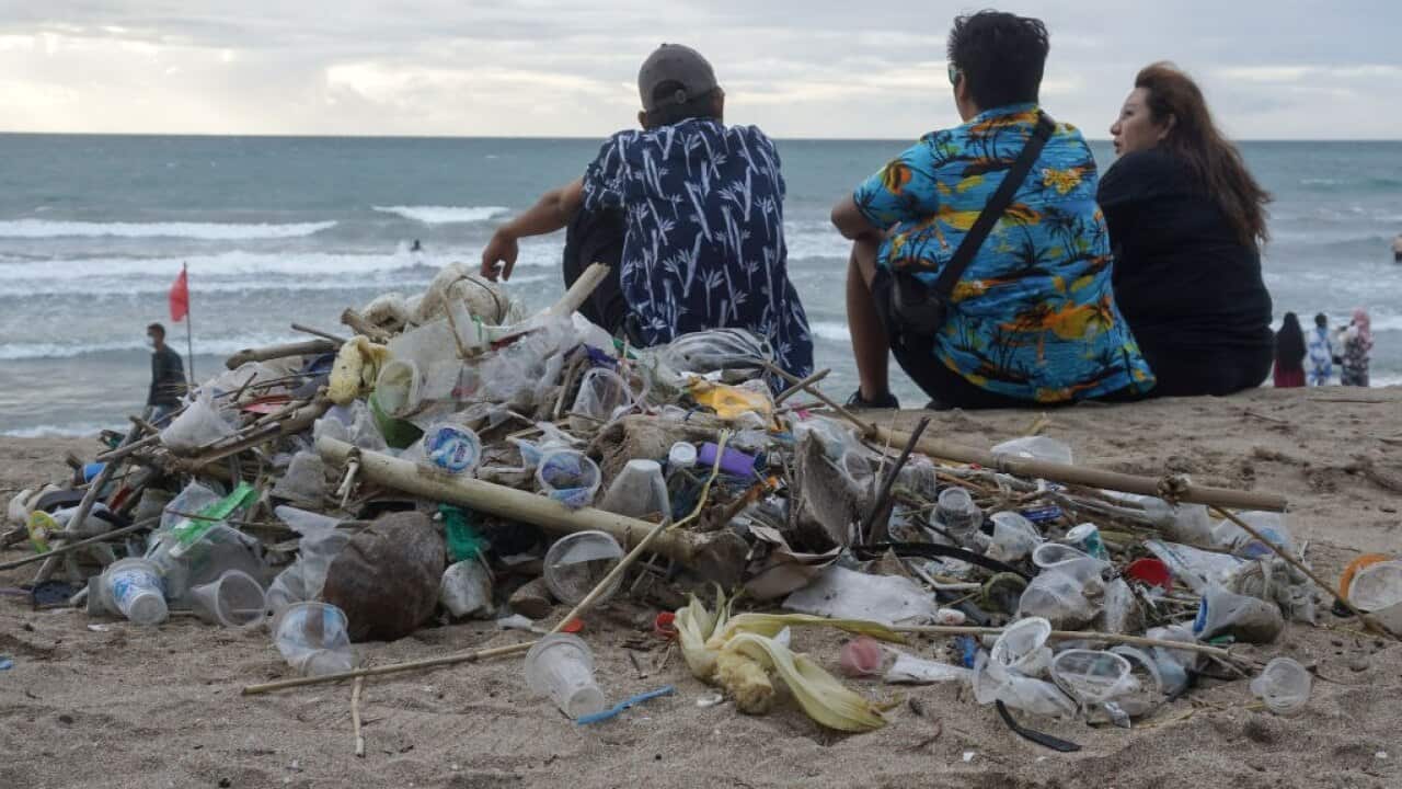 Tourists sit near trashes on Kuta Beach, Bali.