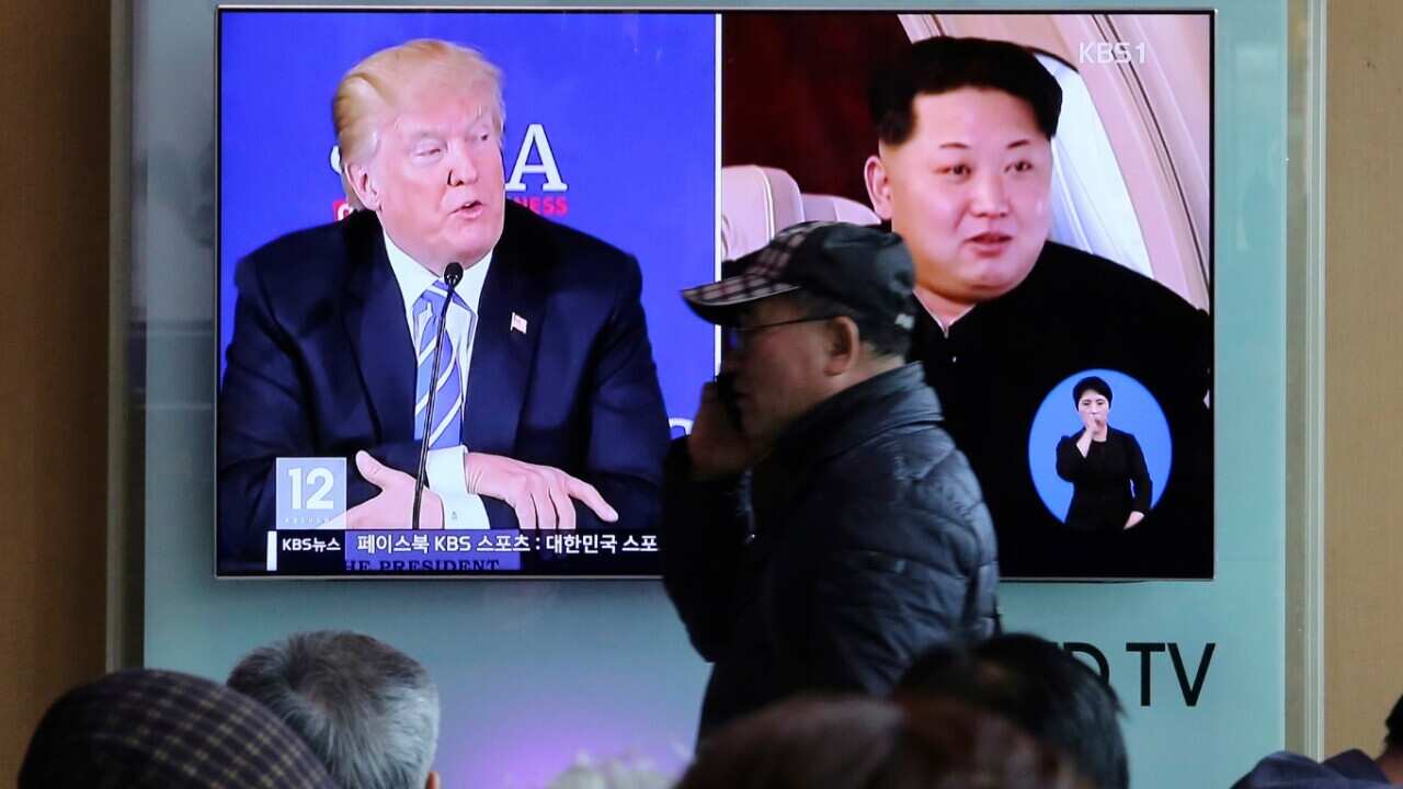 A man passes by a TV screen showing file footage of U.S. President Donald Trump, left, and North Korean leader Kim Jong-un
