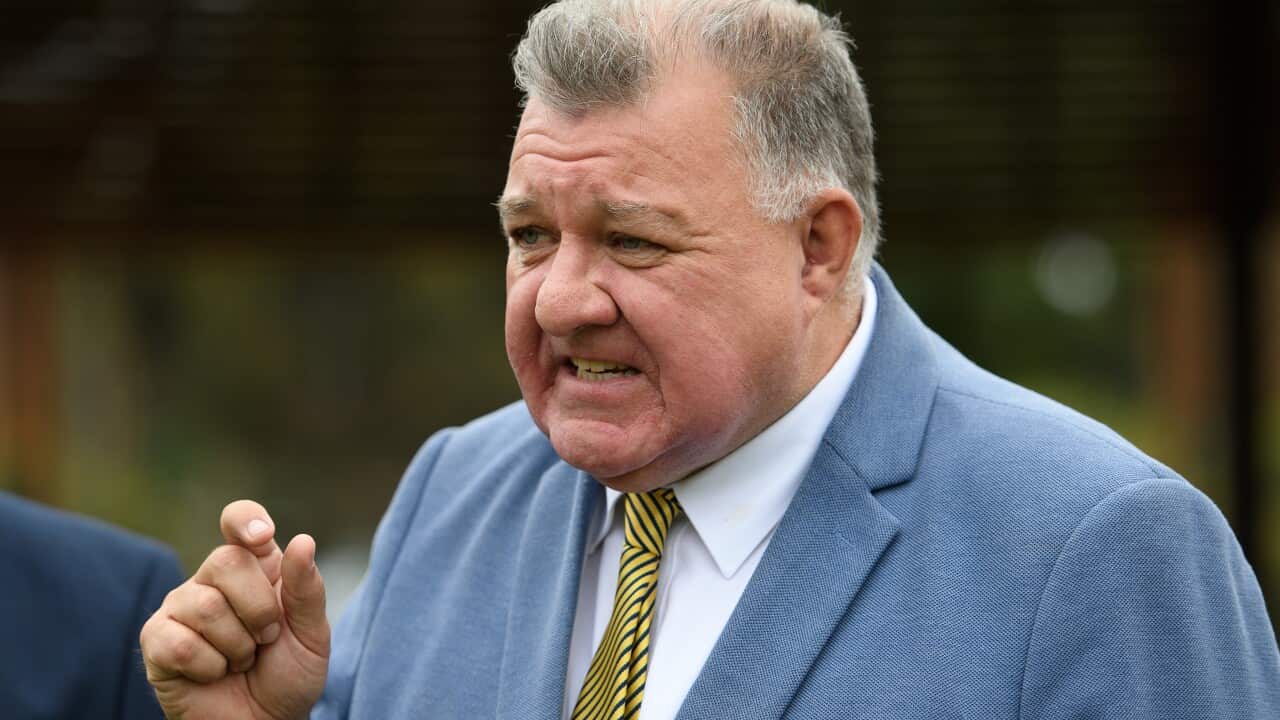 A man wearing a suit and tie speaks emphatically while standing outside.