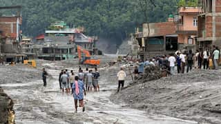 People standing on mud that has swept through a town in Nepal, some buildings remain standing
